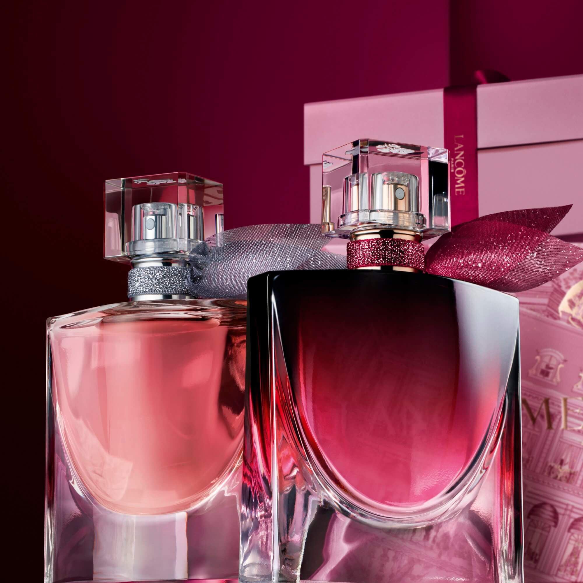 Image of La vie est belle EDP and La vie est belle L'Elixir Very Cherry standing in front of a pile of pink and dark red gift boxes, set against a dark red background. 