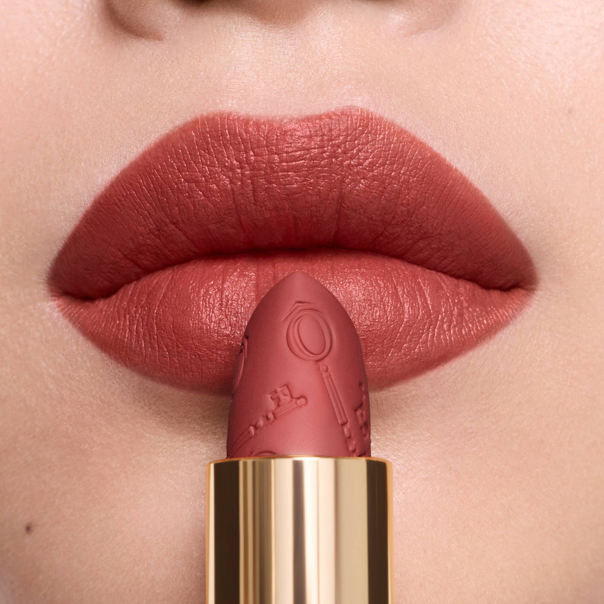 A close-up of warm matte lipstick on lips, beside its matching engraved lipstick bullet.	