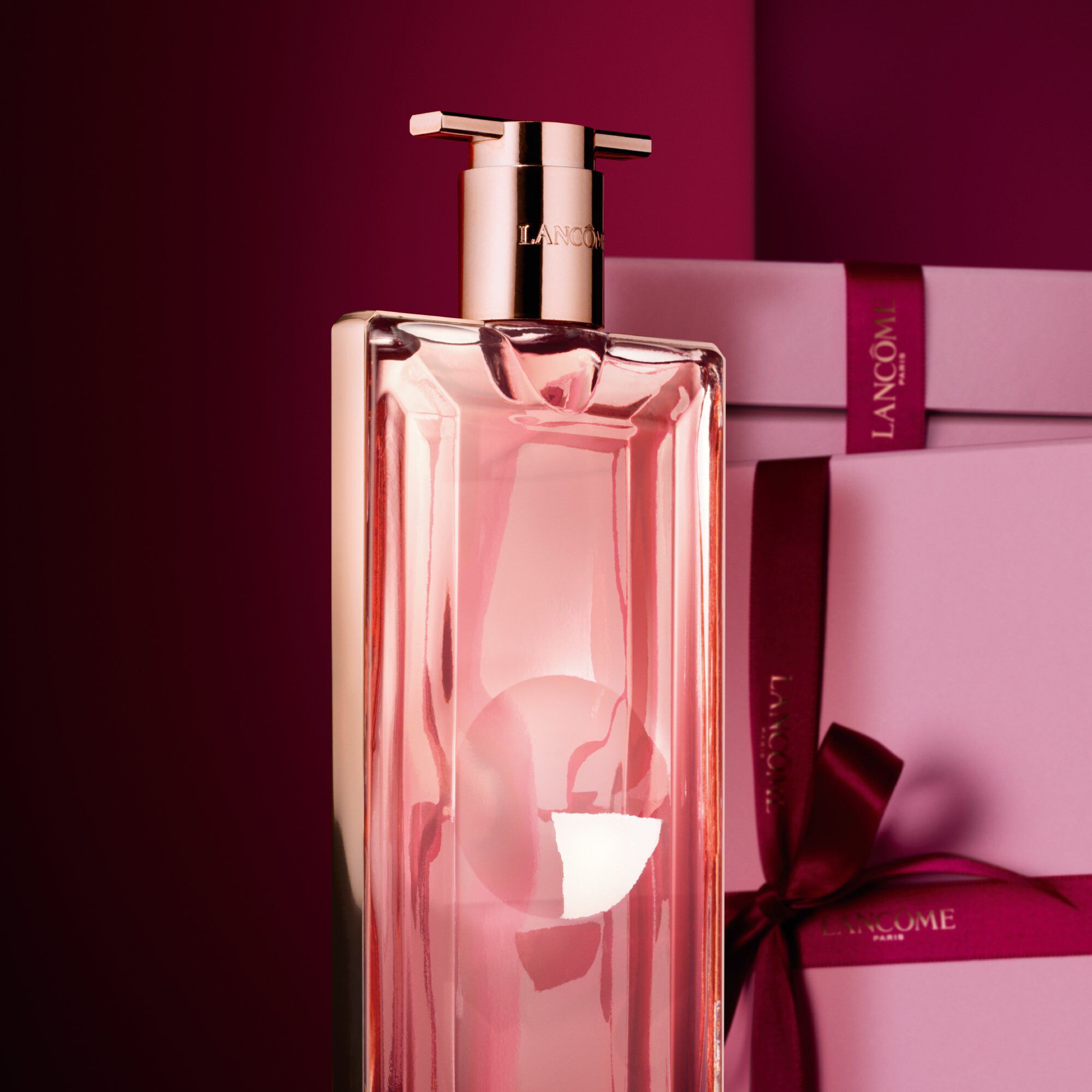 Image of Idole EDP standing in front of a pile of pink and dark red gift boxes, set against a dark red background. 