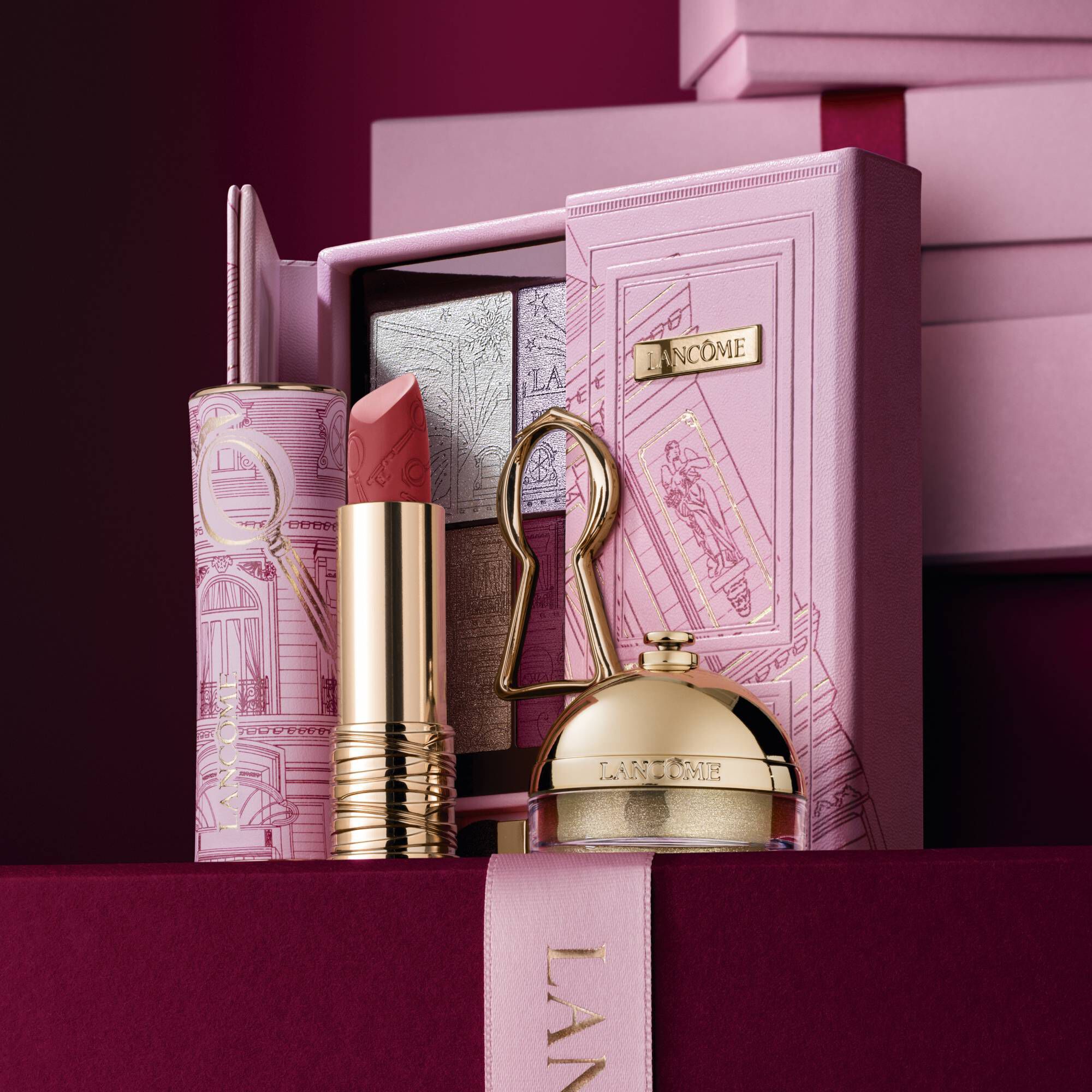 Image of Lipstick Drama matte limited edition, Ring & Shine & The Suite Escape Palette standing in front of a pile of pink and dark red gift boxes, set against a dark red background. 	
